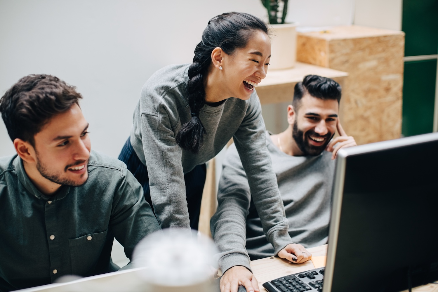 Cheerful colleagues discussing while looking at computer on desk in office